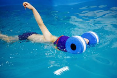 Üç-yıl-yaşlı oğlan mavi bir kap ve yüzme gözlük bir köpük oyuncak kullanarak bir havuzda yüzüyor. Dalış. Sağlıklı bir yaşam tarzı. Aquatherapy. Yüzme rehabilitasyon.