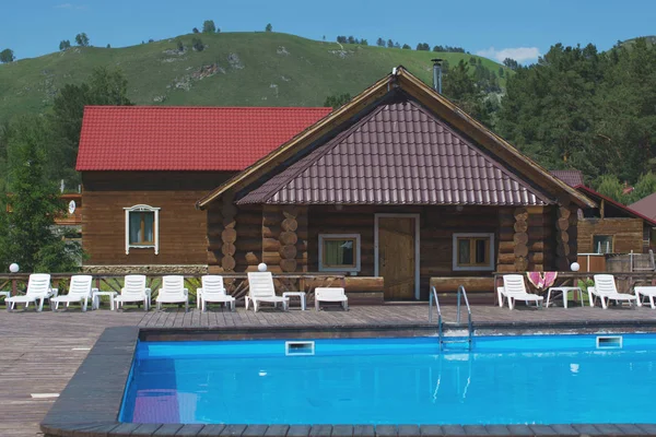Brown Wooden house in a hotel complex with a swimming pool and beach chairs.
