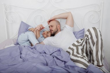 Baba Çizgili Pijama ve bir oğlu mavi yatak ve yastıklar bir beyaz duvara bir yatakta.