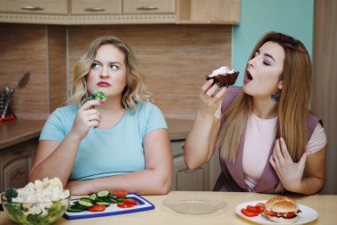 İnce kız cupcake, şişman kızın adını kıskanç yiyor. Diyet, doğru beslenme, sağlıklı yaşam tarzı.