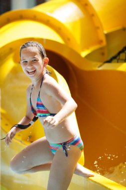 Genç güzel kız bir çizgili renkli mayo güler, aqua park sarı su slayttaki rides.