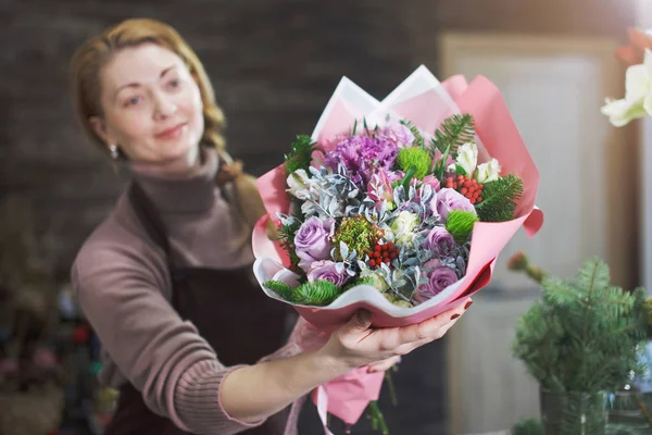 Female florist in a brown apron shows a buyer a beautiful bouquet in the flower salon for a holiday gift for a wedding or anniversary.