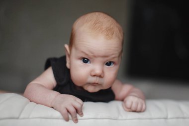 Küçük kel iki aylık bebek kiraz yatak örtüsü üzerinde yatıyor ve kameraya benziyor.