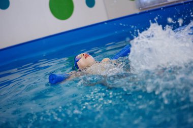 Bir şapka ve yüzme gözlüğü çocukta bir havuzda yüzmek öğrenmektir. Sağlıklı yaşam, su rehabilitasyon, aquatherapy.