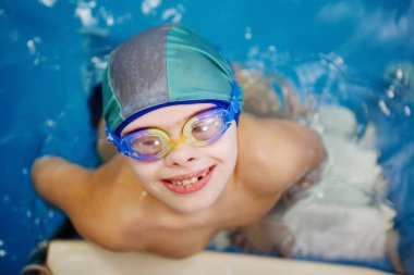 Bir şapka ve yüzme gözlüğü çocukta bir havuzda yüzmek öğrenmektir. Sağlıklı yaşam, su rehabilitasyon, aquatherapy.