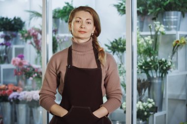 Çiçekçi Çiçek salonu önünde çiçek demetleri ile buzdolabı kahverengi önlük kadında. Seçilen odak, arka plan bulanık.