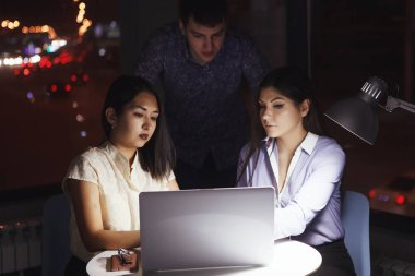 Bir gece ofiste dizüstü bilgisayar ile bir masada oturan ve çizelgeleri sayfaya bakarak üç meslektaşları. Ekip çalışması, son tarih, acil çiçek.