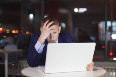 Masada laptop ile çalışma gece ofiste iş adamı. Pencerenin dışında çeşitli renklerde ışık yanıyor. Son Tarih, fazla mesai.