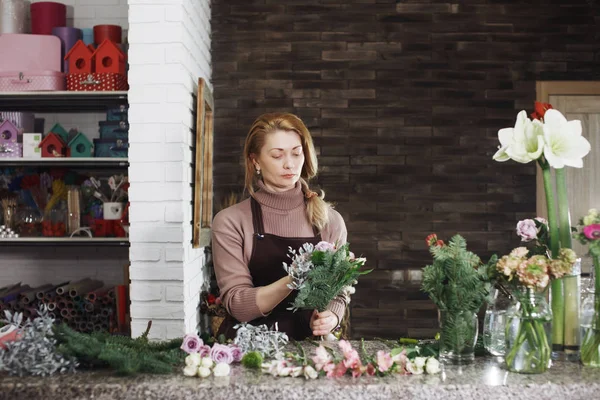 Pretty middle-aged florist woman in apron makes a bouquet in the flower salon for a festive gift for a wedding or anniversary.