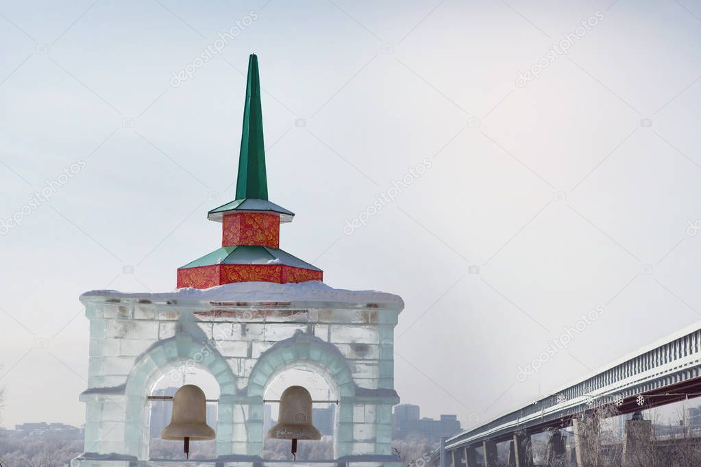 Ice gate with a sharp spire and bells on the river bank near the bridge.