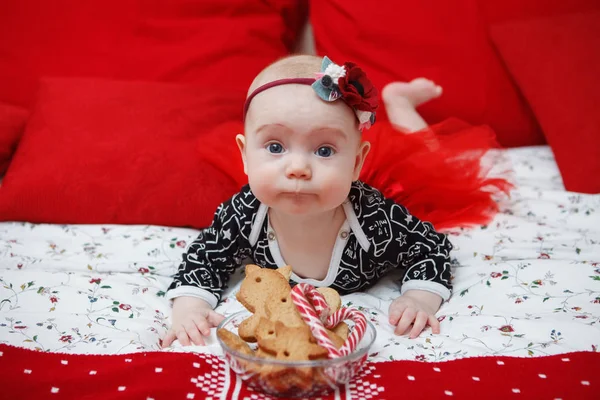 背景が赤でクリスマスのジンジャーブレッドと青いドレスの彼女の頭の上の花の美しい ヶ月の赤ちゃん幼児の女の子 母の介護 子供の世話 クローズ アップ — ストック写真