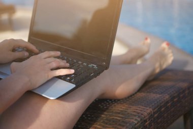 Genç Sevimli Kadın yakınındaki bir havuz mavi su resort otel ile bir dizüstü bilgisayar ile çalışıyor. Eller ve ayaklar kırmızı çivi yakın çekim ile.