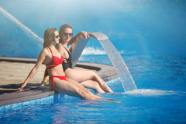 Havuzda bir çeşme ile açık mavi su resort otel yakınındaki iki genç güzel kadın uzun saçlı oturmak.
