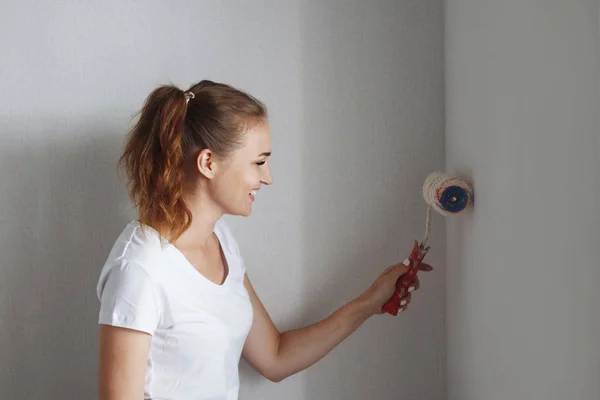 Young woman in white T-shirt painting wall with roller in new apartment