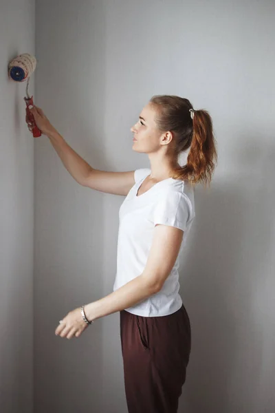 beautiful woman in white T-shirt painting wall with roller in new apartment