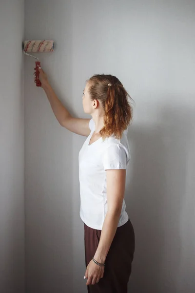 Young woman in white T-shirt painting wall with roller in new apartment