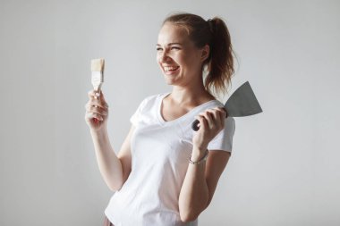 Onarım sırasında poz boya fırçası ve yeni dairede spatula ile beyaz tişört içinde genç kadın