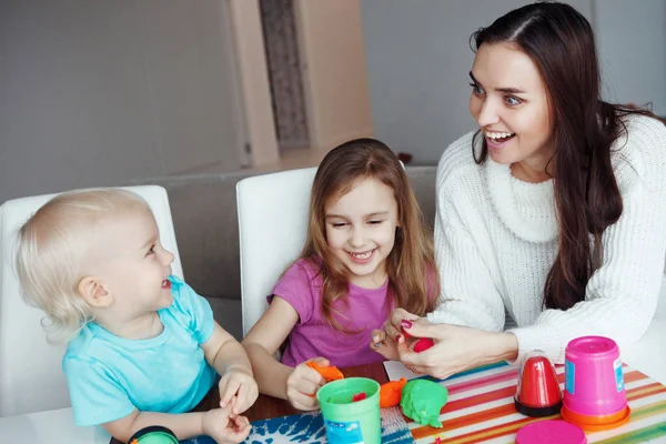母亲与儿子和女儿玩塑料坐在家里的桌子上 — 图库照片