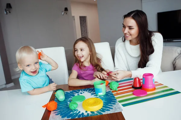 Anne ile oğlu ve kızı evde masada oturan hamuru ile oynamak