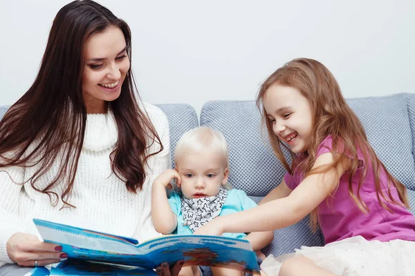 mother with son and daughter sitting on couch and reading book at home