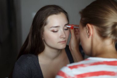 Makyaj Ustası genç kadının yüzünde kaşları şekil modelleme