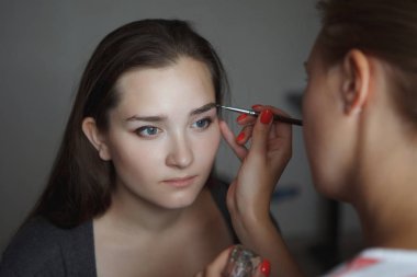 Makyaj Ustası genç kadının yüzünde kaşları şekil modelleme