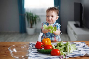 Sevimli küçük çocuk masada yeşil, sarı ve kırmızı sebze salatası hazırlama