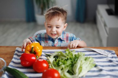 Sevimli küçük çocuk masada yeşil, sarı ve kırmızı sebze salatası hazırlama