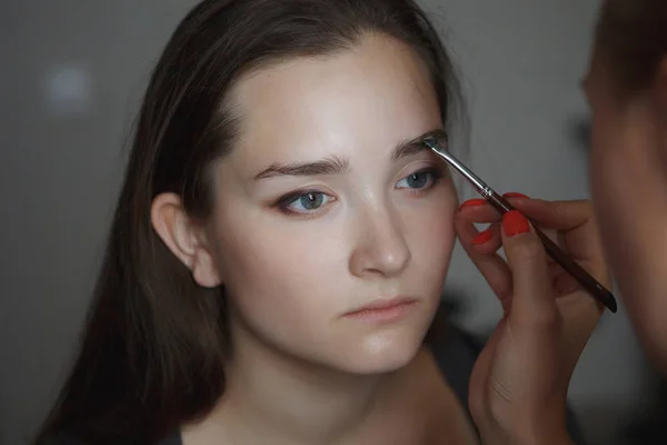 makeup master modeling shape of eyebrows on face of young woman