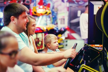 Anne, baba, genç kız ve küçük çocuk eğlence parkı oyun makinesi araba arcade sürüş