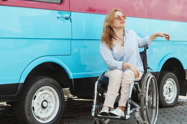 Woman in wheelchair next to blue bus smiling and posing at camera