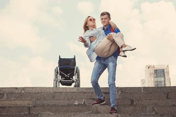 young man carrying disabled woman on steps of stone staircase