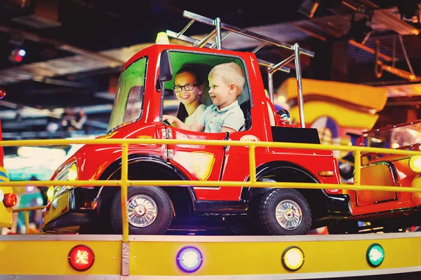 可爱的少女和小男孩骑在旋转木马在玩具汽车街机在游戏机在游乐园 — 图库照片