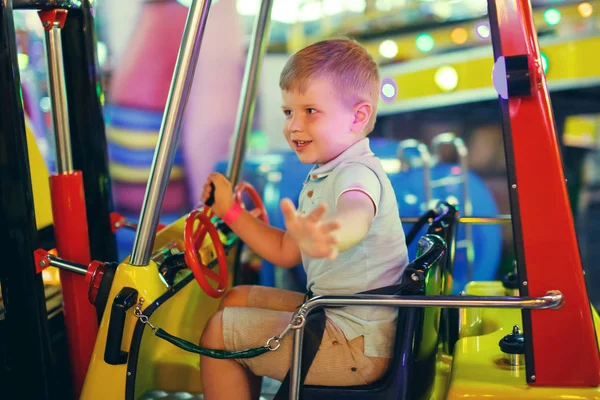 遊園地でのおもちゃの車のカルーセルに乗って青い シャツにかわいい男の子 — ストック写真