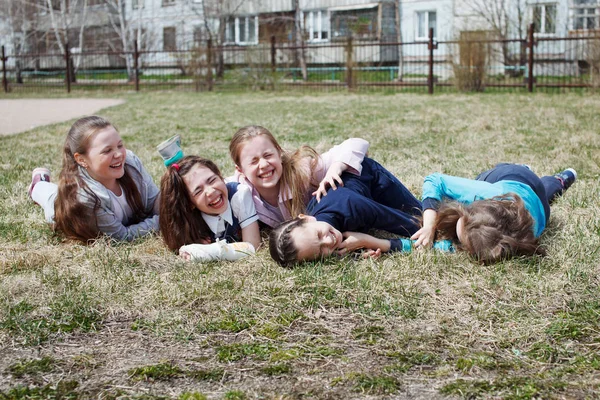 Um grupo de crianças sorri, diverte-se, deita-se em um gramado verde. O conceito de lazer infantil, estilo de vida saudável . — Fotografia de Stock