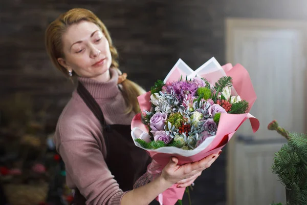 Female florist in a brown apron shows a buyer a beautiful bouque