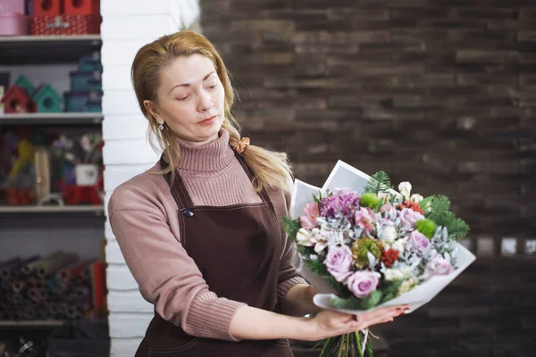 Pretty middle-aged florist woman in an apron collects a bouquet. — Stock Photo, Image