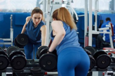 Genç, uzun saçlı, halterleri kaldıran güzel bir kız..