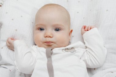 Sırtı, farklı duygular ve yüzünde bir gülümseme güzel beş aylık mavi gözlü Bebek Tulum içinde yatıyor. Bebek bak. Anne bakım. Çocuk Bakımı. Yakın çekim.