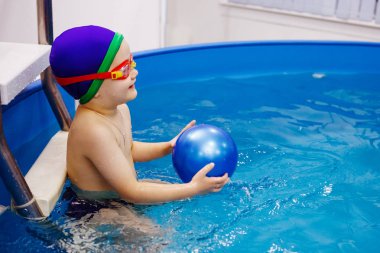 Mavi şapkalı ve gözlüklü çocuk havuzda yüzüyor..