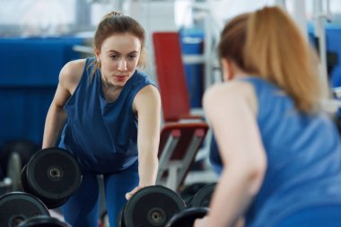 Genç, uzun saçlı, halterleri kaldıran güzel bir kız..