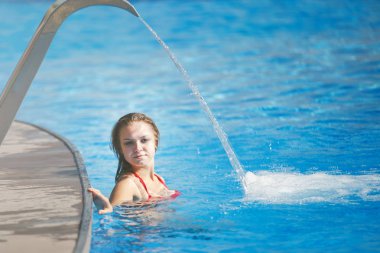 Berrak blu ile bir havuzda bir şelale altında genç güzel kadın