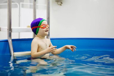 Mavi şapkalı ve gözlüklü çocuk havuzda yüzüyor..