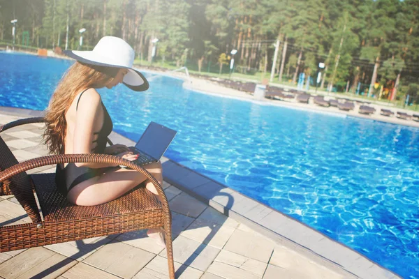 Jonge mooie vrouw in een zwart badpak werkt met een laptop — Stockfoto