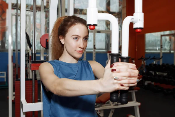 Genç ve güzel bir kadın spor salonundaki simülatörde fiziksel egzersiz yapıyor..