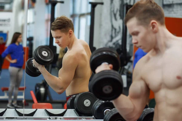 Jeune homme athlétique soulevant des haltères dans la salle de gym . — Photo