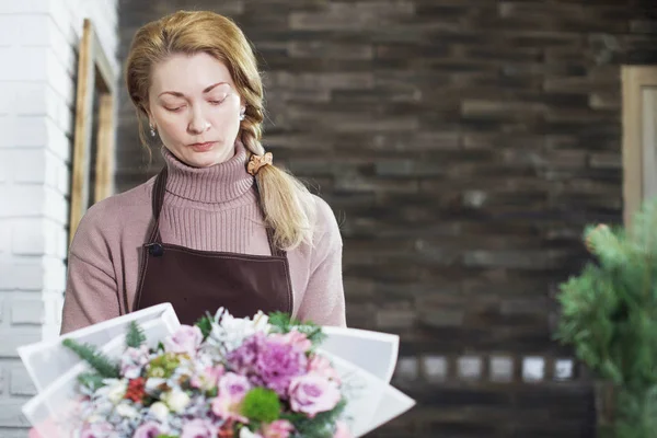 Pretty middle-aged florist woman in an apron collects a bouquet. — Stock Photo, Image