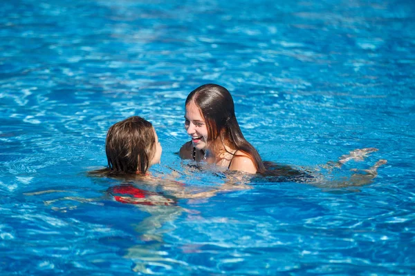 Dos mujeres guapas jóvenes nadan en la piscina con agua azul clara en el complejo hotelero . — Foto de Stock