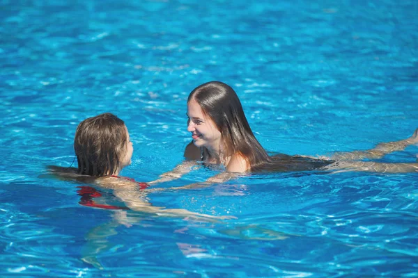 Dos mujeres guapas jóvenes nadan en la piscina con azul claro — Foto de Stock