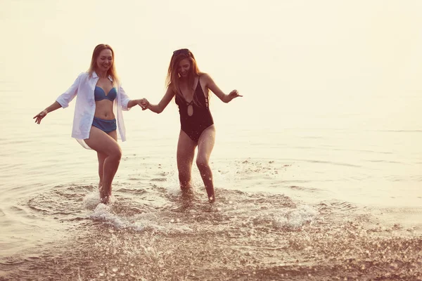 Dwie dziewczyny bawią się w morzu o zachodzie słońca. — Zdjęcie stockowe